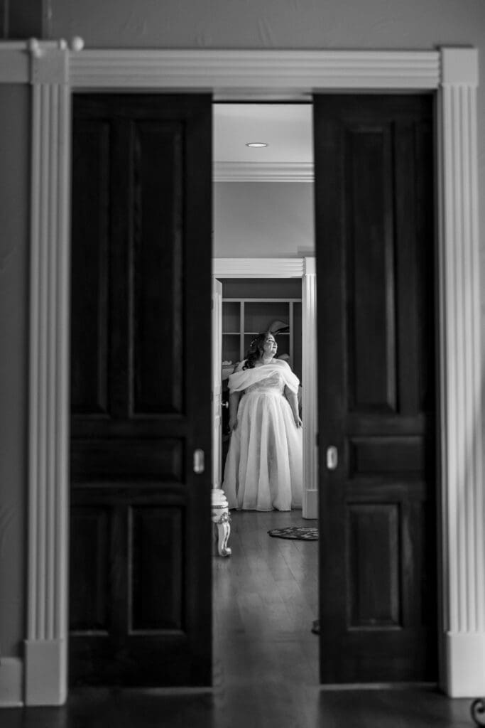 The bride looks out the window while her MOH corsets her dress at the Dempsey Event Center in Delaware, Ohio.