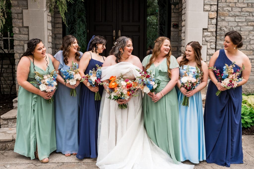 The bride and her bridesmaids dressed in shades of blue and green holding colorful wildflower bouquets at the Dempsey Event Center in Delaware, Ohio.