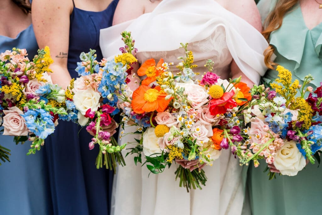 The bride and her bridesmaids dressed in shades of blue and green holding colorful wildflower bouquets at the Dempsey Event Center in Delaware, Ohio.