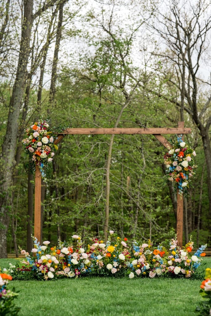 Wooden arch with colorful wildflowers ceremony setup at the Dempsey Event Center in Delaware, Ohio.