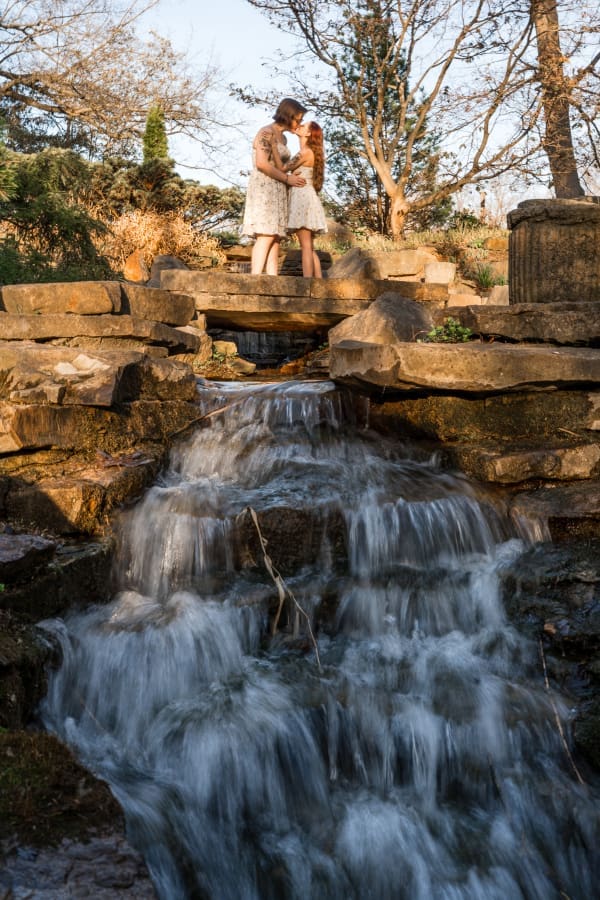 An LGBTQ+ engagement session of the couple kissing above a mini waterfall at Inniswoods Metro Gardens.