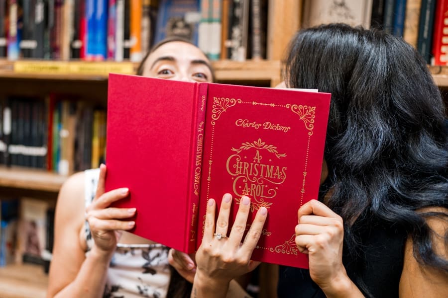 Couple holding up "A Christmas Carol" book during their Couple sitting amongst the stacks for their engagement session at the Book Loft in Columbus, Ohio.